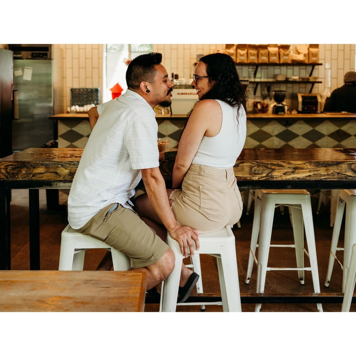 Couple on stools at a cafe counter turned toward each other, faces close and smiling