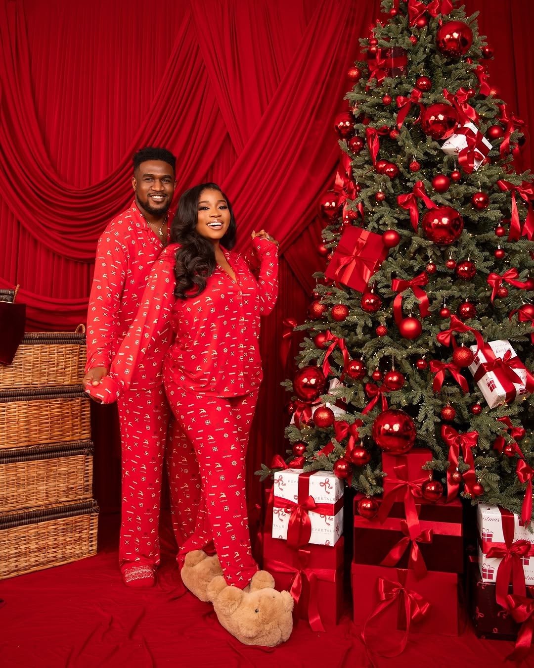 Smiling couple in Christmas pyjamas beside pile of wrapped gifts