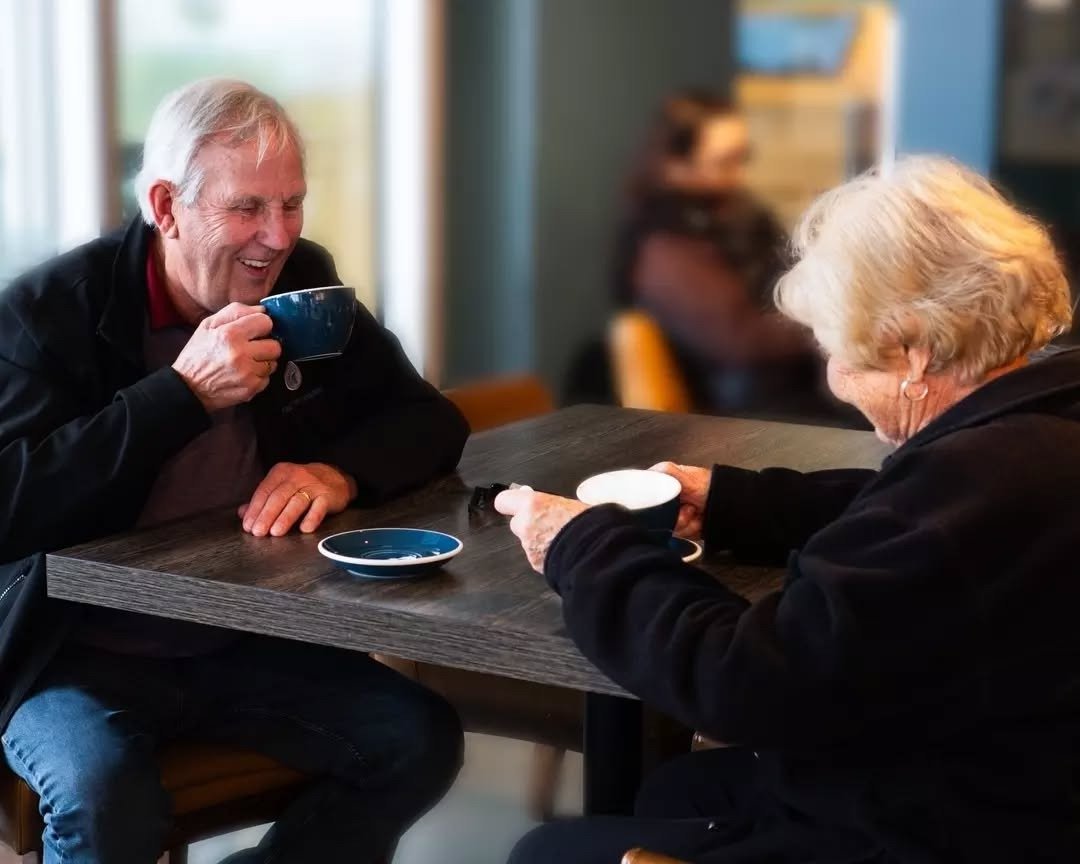 Older couple laughing over coffee at a cafe table