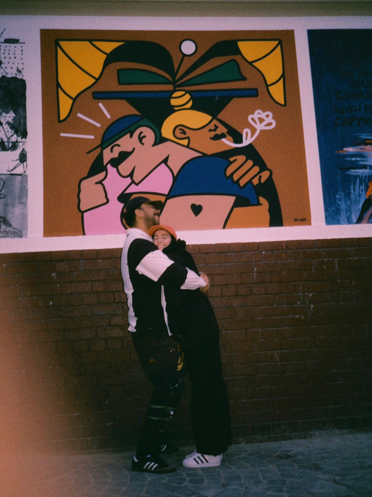 Couple hugging in front of a colorful mural