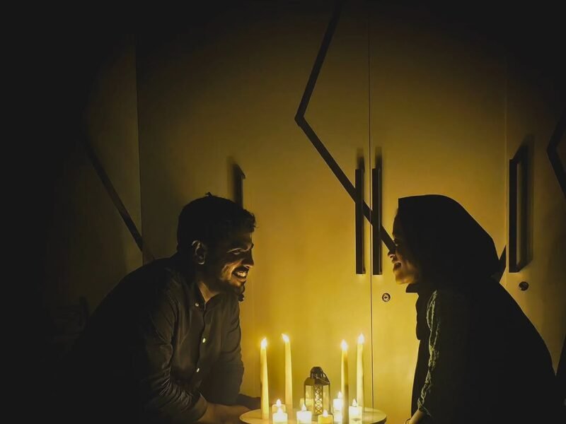 Couple at a small candlelit table at home, dark room glowing with candles
