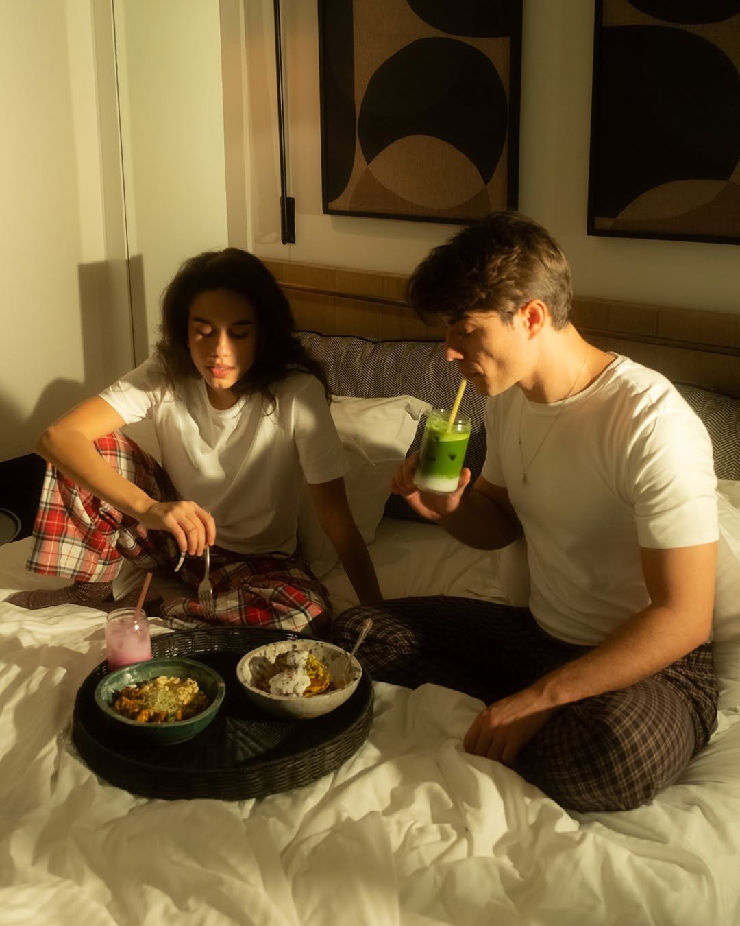 Couple in pyjamas sharing breakfast from a tray in bed in morning light