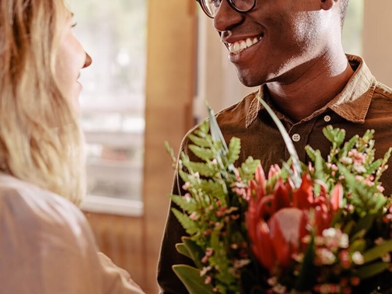 Man presenting red bouquet to woman at home