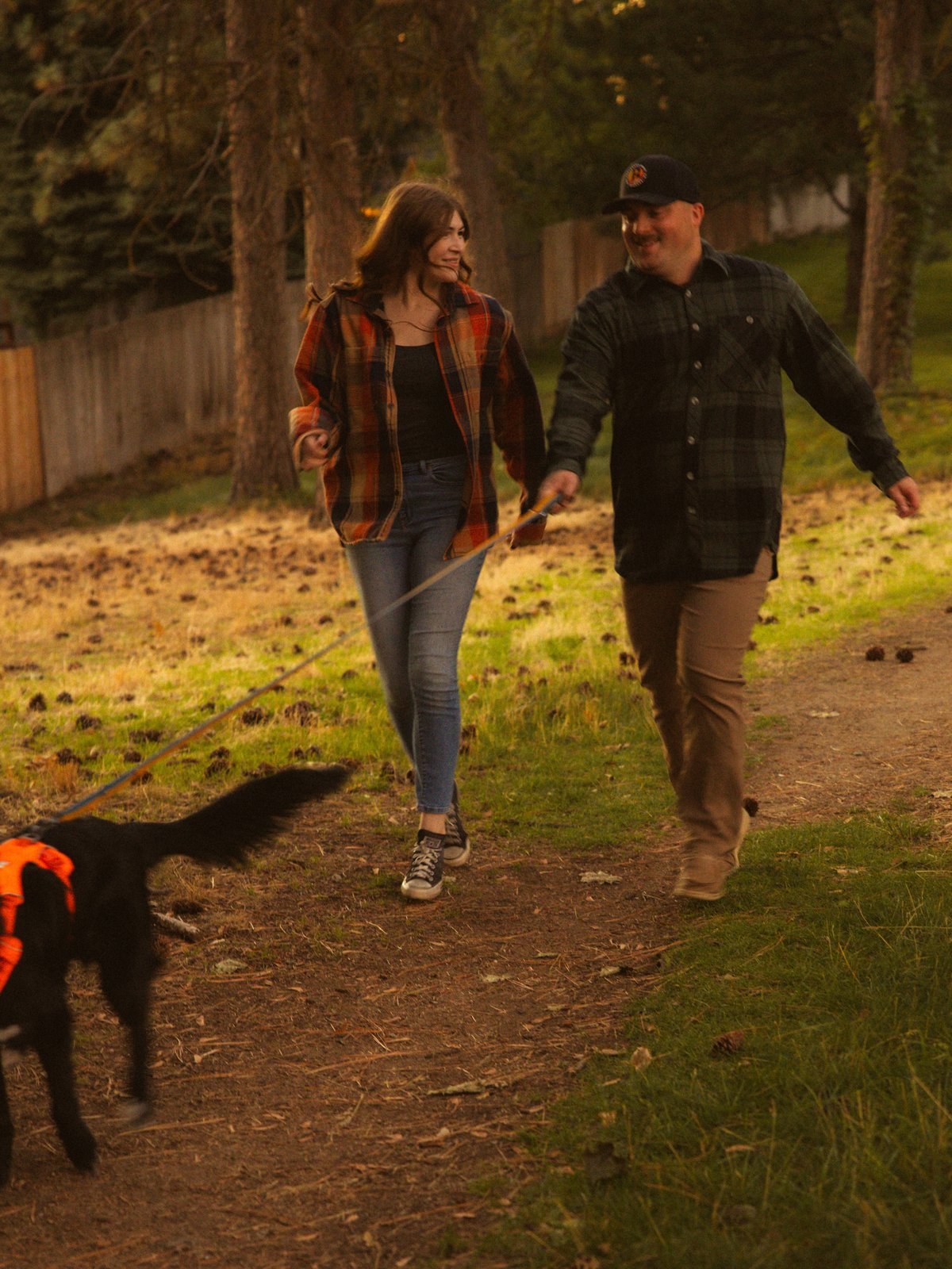 Couple walking their dog on a park path, laughing together