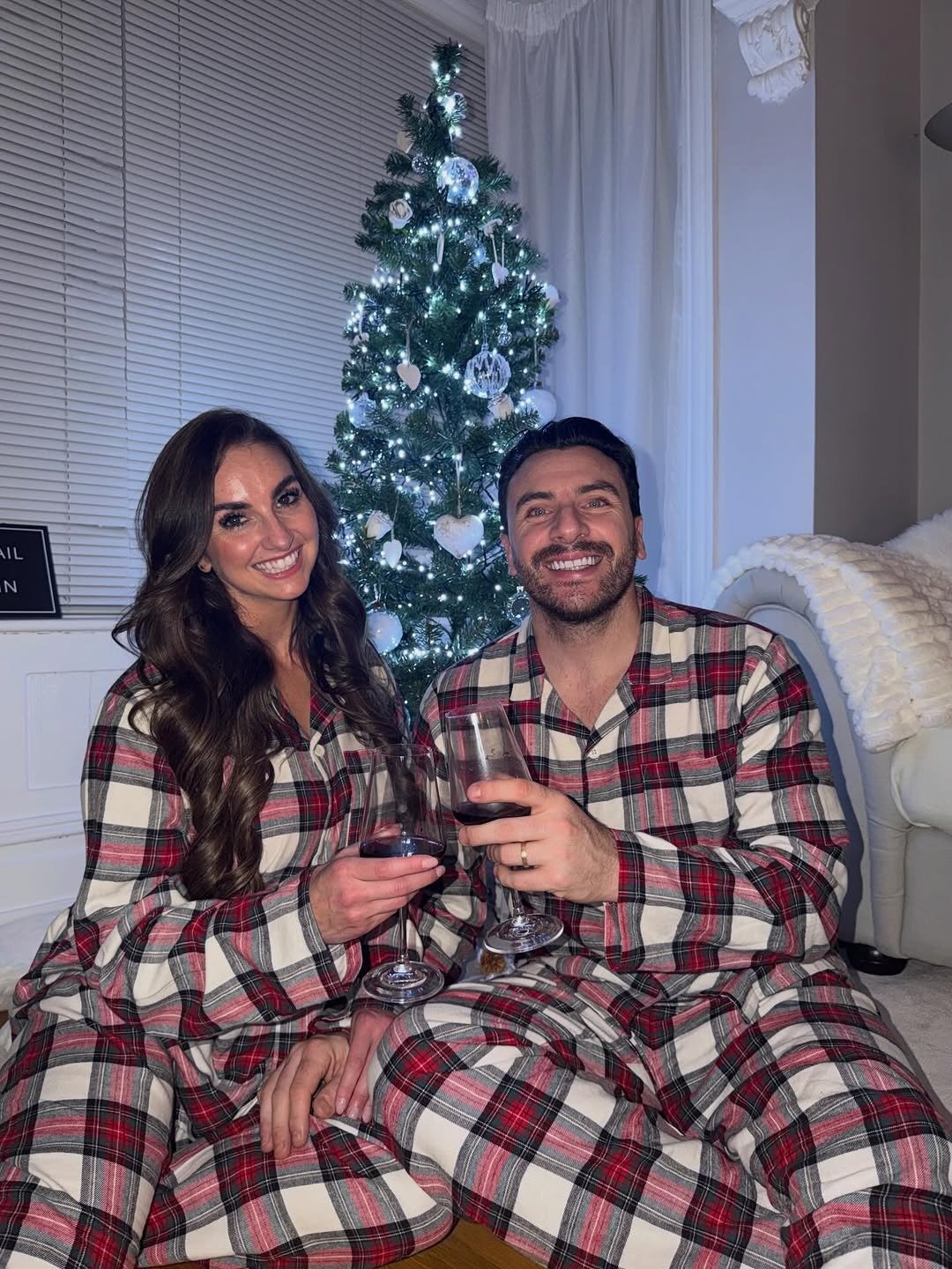 Couple in matching plaid Christmas pajamas by tree