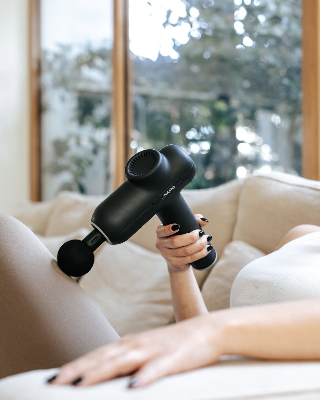 Person using mini massage gun on thigh on couch