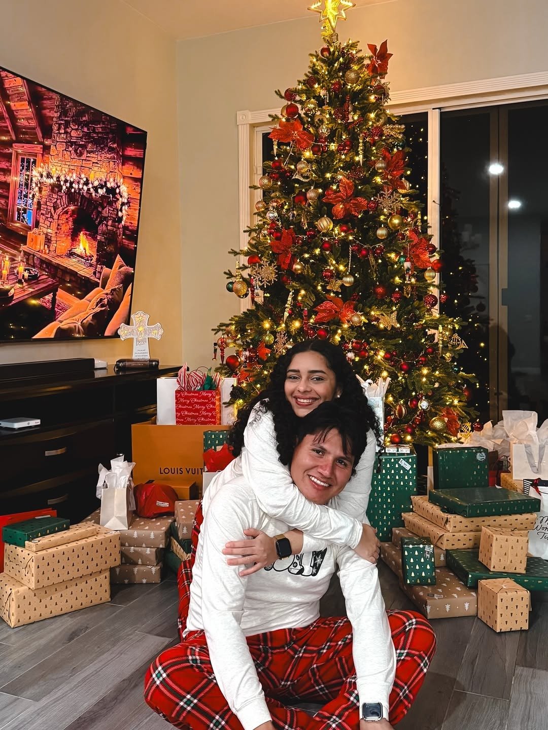 Couple in Christmas pajamas embracing among wrapped gifts by tree, from our christmas gift guide